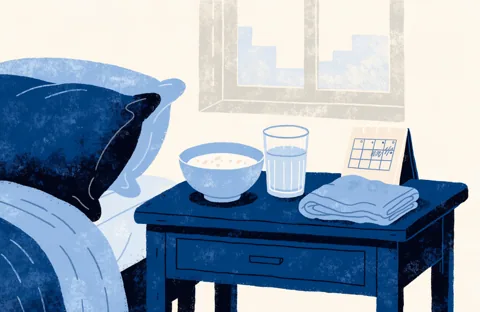 A home recovery scene: a bowl of soup, a glass of water, a folded blanket and a small calendar on a bedside table.